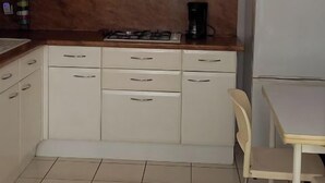 Eine kleine Küche mit weißen Schränken, einem Gasherd, einer Kaffeemaschine und einem Kühlschrank.