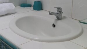Ein Badezimmer mit einem weißen Waschbecken, einem Spiegel mit türkisfarbenen Akzenten und einem Glastischchen.
