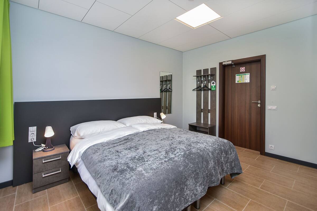 A hotel room with a bed, bedside lamp, nightstand, and a door with a sign.