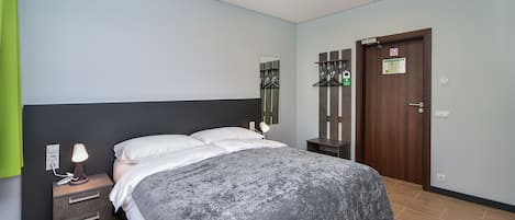 A hotel room with a bed, bedside lamp, nightstand, and a door with a sign.