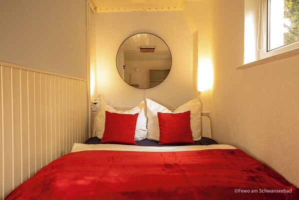 A bedroom with a bed, a round mirror, and a window.