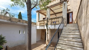 Une cour intérieure avec un escalier menant à un balcon, le tout entouré de murs en pierre et d’un arbre.