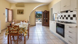 Une cuisine équipée d’une cuisinière, d’un four et de placards. On y trouve une table à manger avec des chaises et une fenêtre.