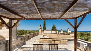 Une terrasse couverte offrant une vue sur la mer, agrémentée d’une balustrade en pierre et d’une table en bois.