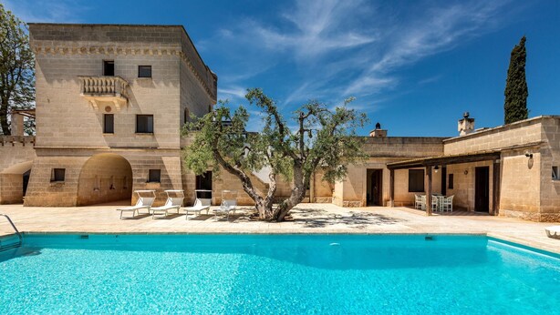 Un espace piscine avec une eau d’un bleu limpide, un arbre et un bâtiment doté d’un balcon.