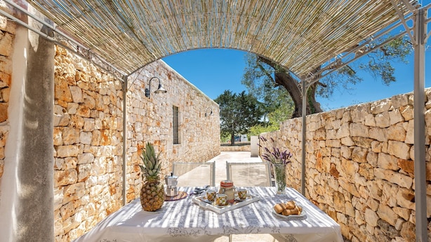 A stone-walled outdoor dining area with a table set for two, featuring a pineapple and bread. - Il Trullo di Erna by BarbarHouse (Ostuni)