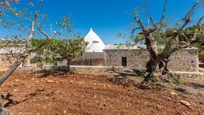 A stone building with a white dome, surrounded by trees and dry ground. - Il Trullo di Erna by BarbarHouse (Ostuni)