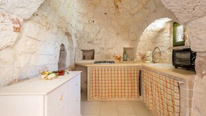 A rustic kitchen with stone walls, a tiled backsplash, and a small window. - Il Trullo di Erna by BarbarHouse (Ostuni)