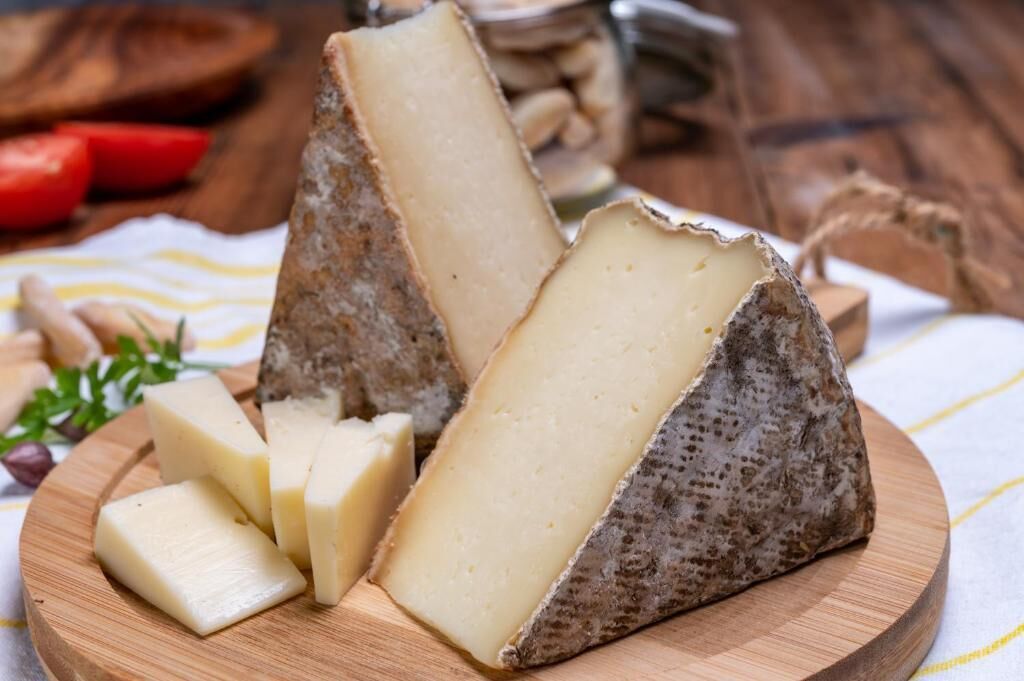 A wooden cutting board with a wedge of cheese and a wedge of cheese with rind.