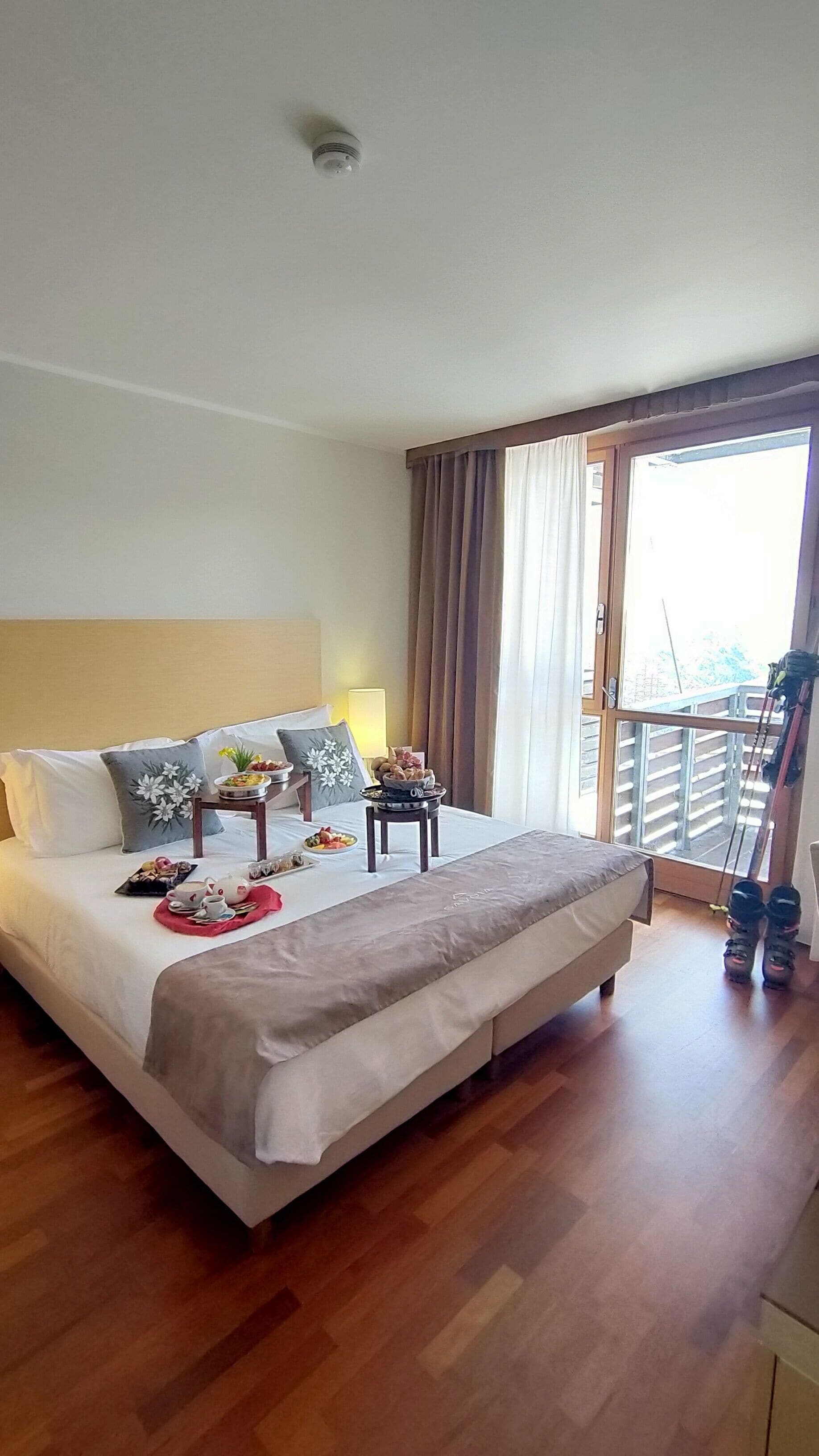 Habitación de hotel con una cama grande, dos mesitas de noche, una ventana con cortinas y un balcón con equipo de ejercicio.