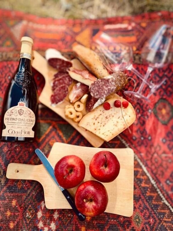 Una tabla de embutidos con diversos quesos, carnes y frutas, una botella de vino, y una tabla con manzanas.