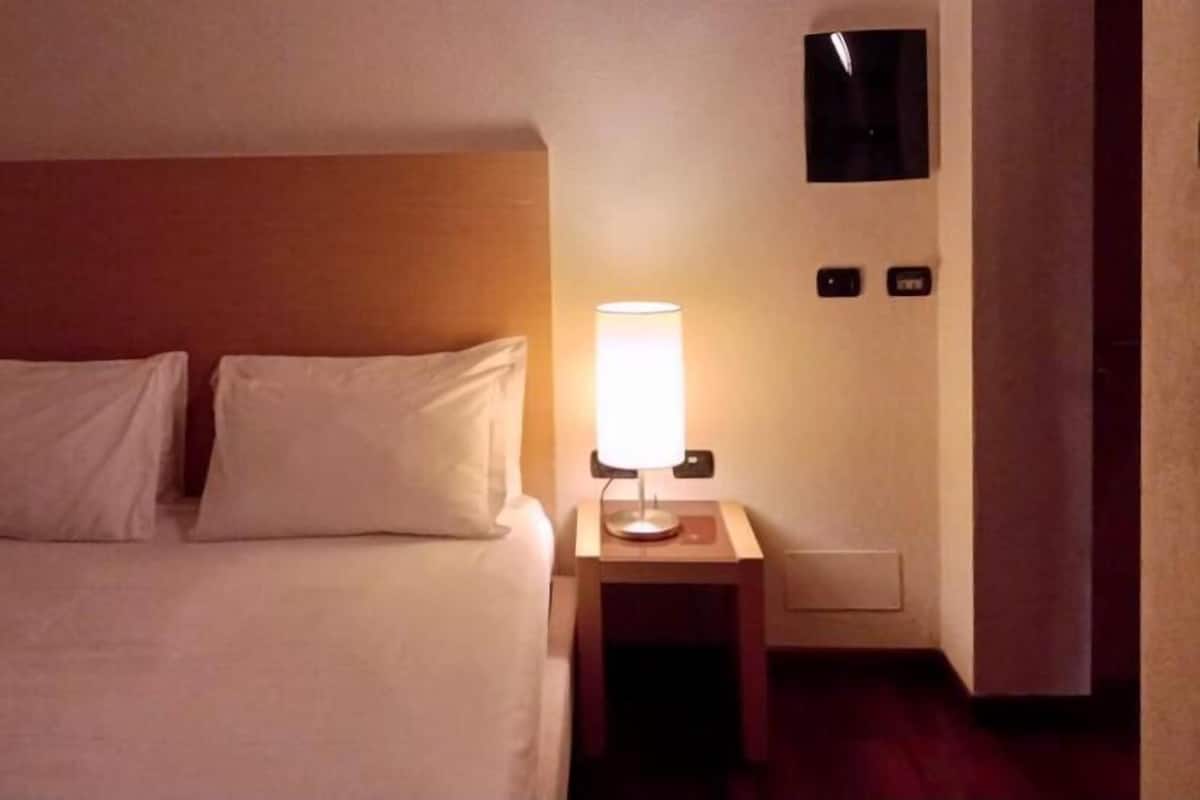 Une chambre d’hôtel avec un lit, une table de chevet, une lampe et un téléviseur fixé au mur.