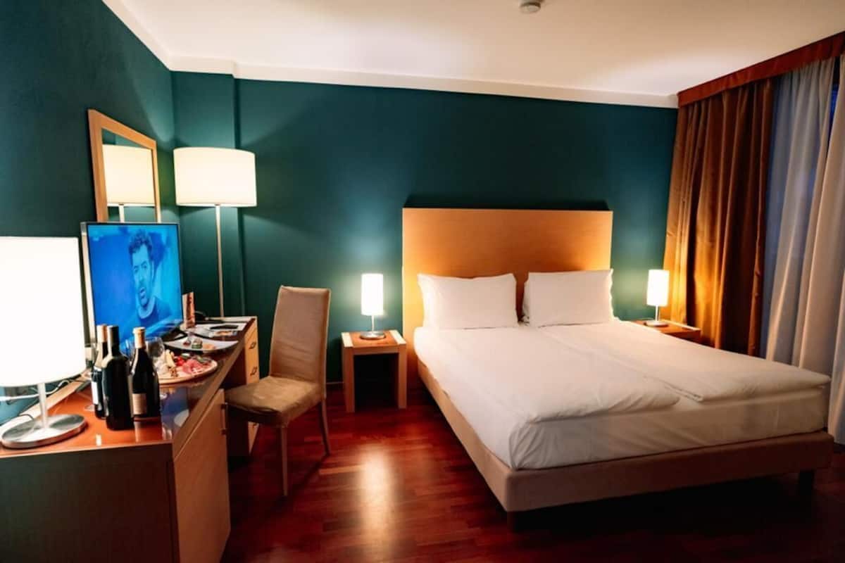 Une chambre d’hôtel avec un grand lit, un bureau avec une chaise, une télévision et deux lampes de chevet.