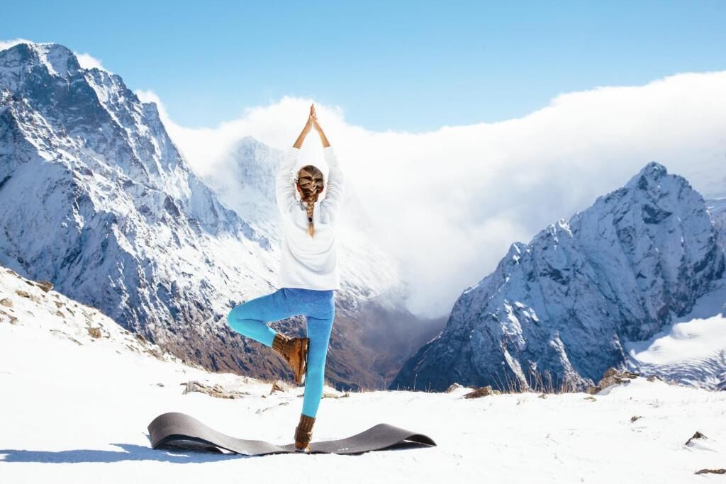 A person performing a yoga pose on a mat in a snowy mountainous area.