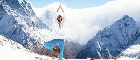 A person performing a yoga pose on a mat in a snowy mountainous area.