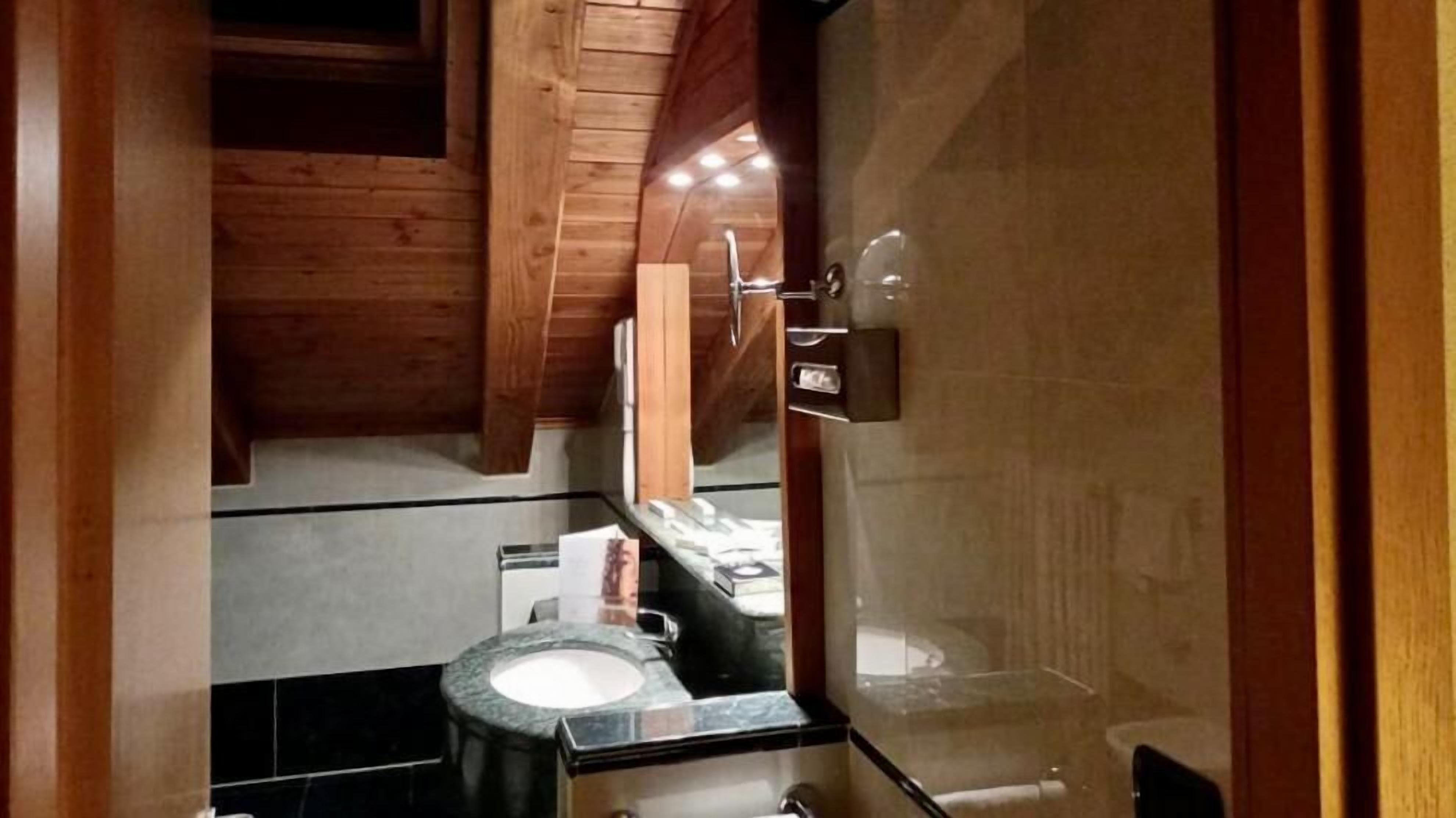 A modern bathroom with a wooden ceiling, a glass shower enclosure, and a marble sink.