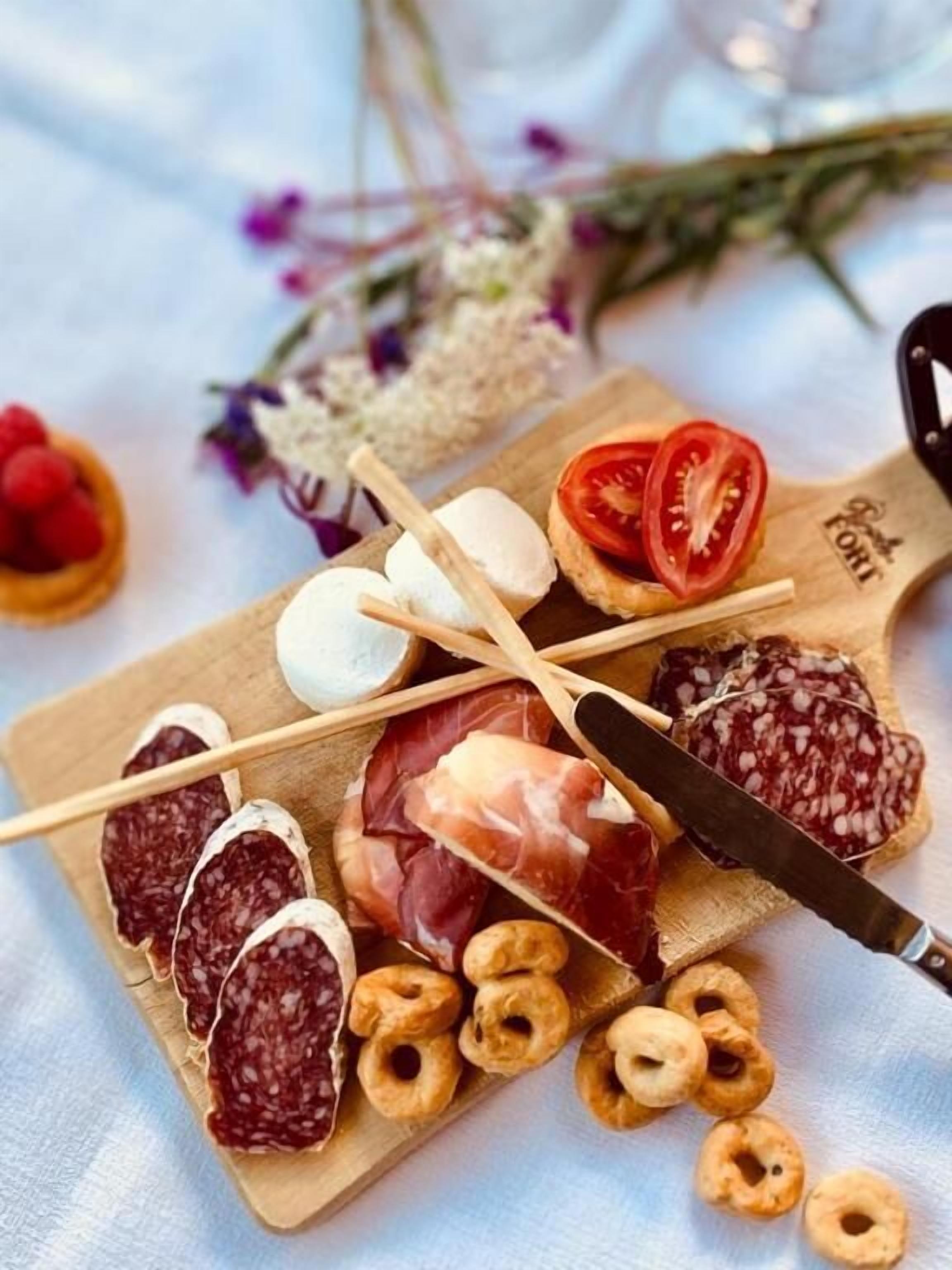 Una tabla de madera con diversos alimentos, como salami en rodajas, prosciutto, tomates cherry y queso.