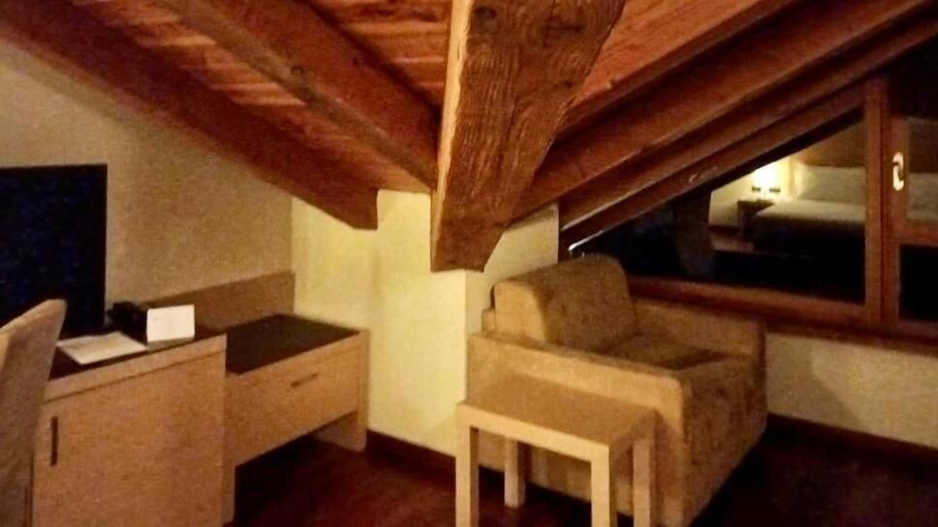 Un pequeño dormitorio en el ático con techo de madera, una cama, un escritorio y una silla.