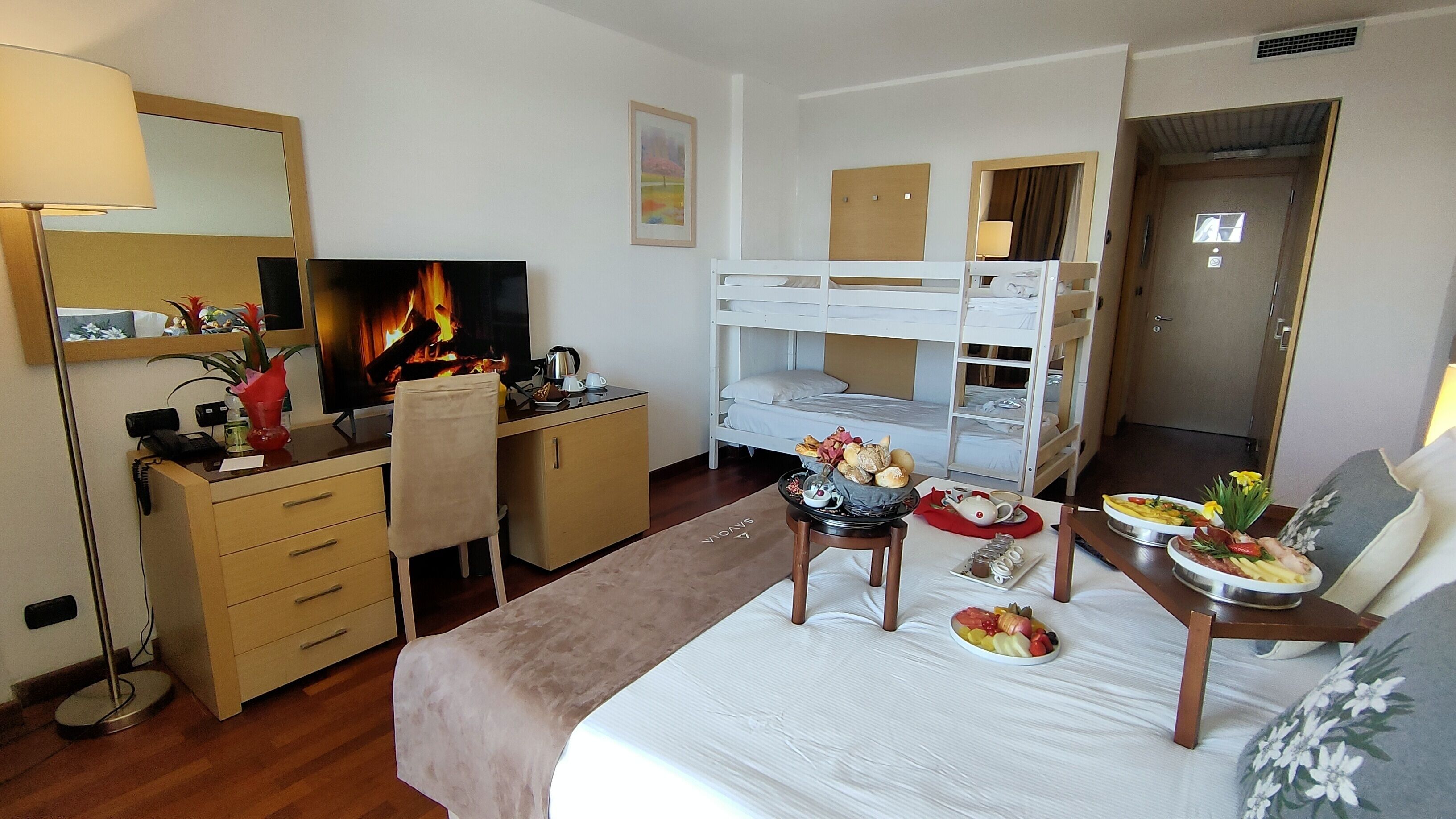 Une chambre d’hôtel comprenant un lit, des lits superposés, un bureau, une chaise, une télévision et une table à manger avec de la nourriture.