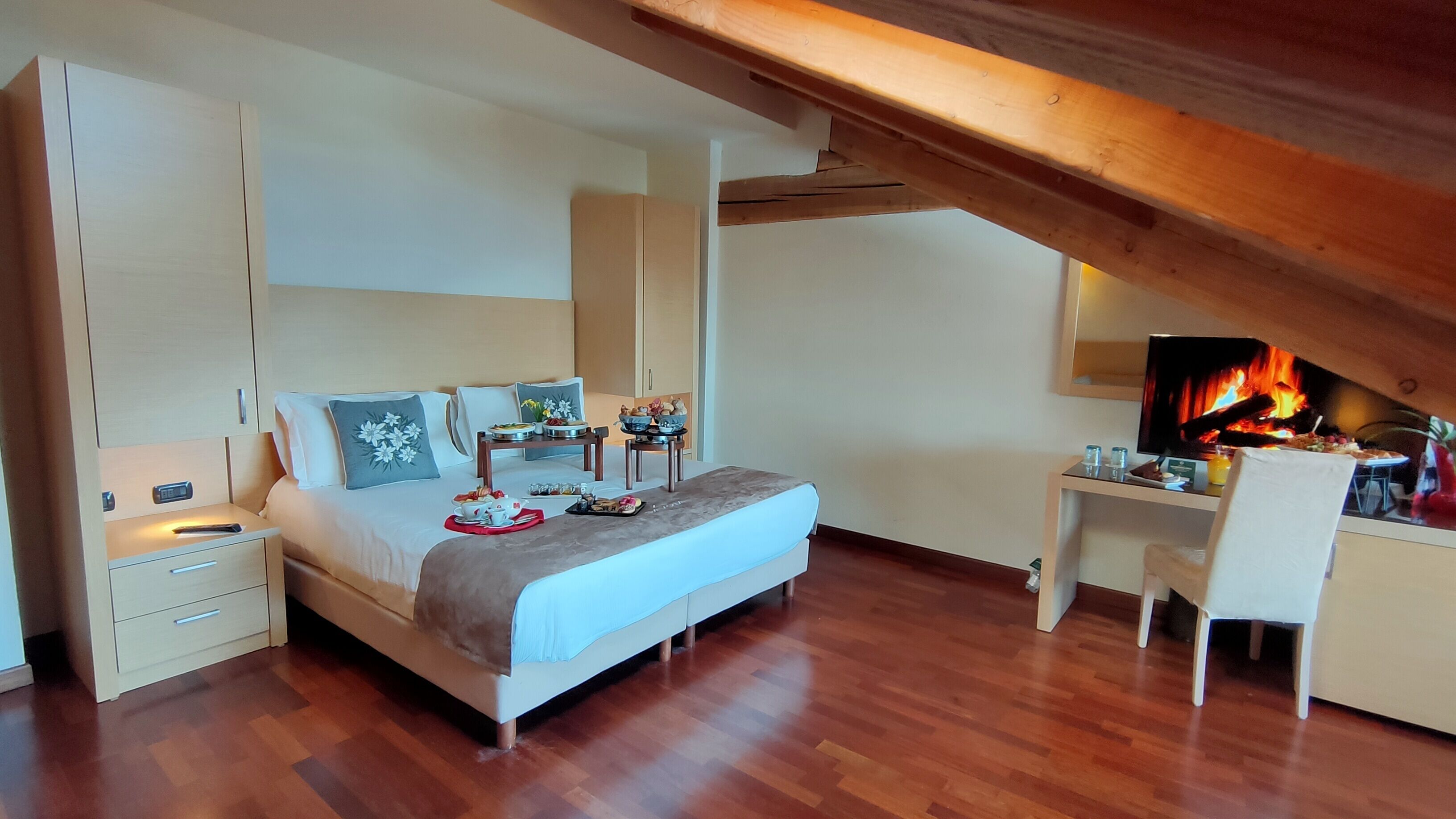 A bedroom with a bed, bedside tables, a desk, and a fireplace.