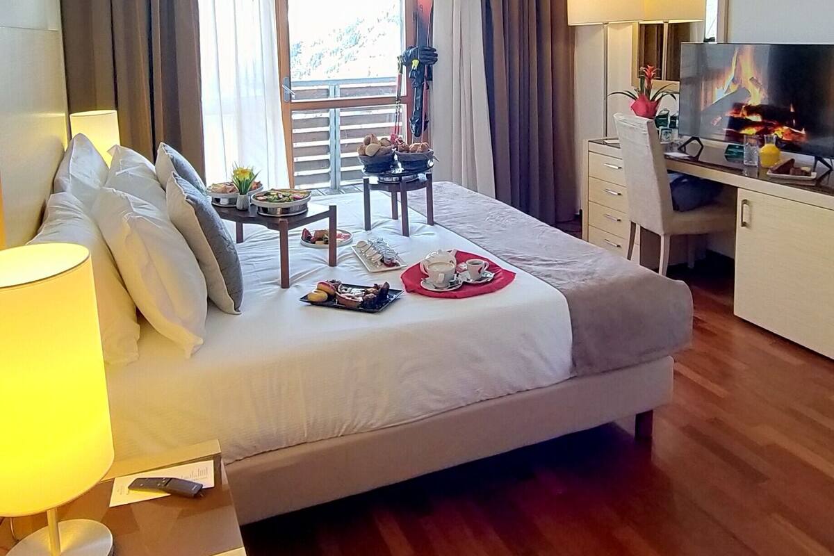 Une chambre d’hôtel avec un lit, un bureau avec une télévision, une chaise et une table avec de la nourriture et des boissons.