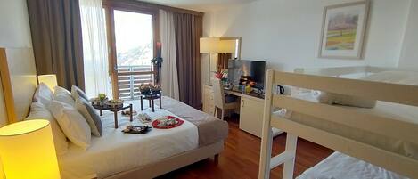 A hotel room with a bed, a desk with a TV, a balcony with curtains, and a painting on the wall.