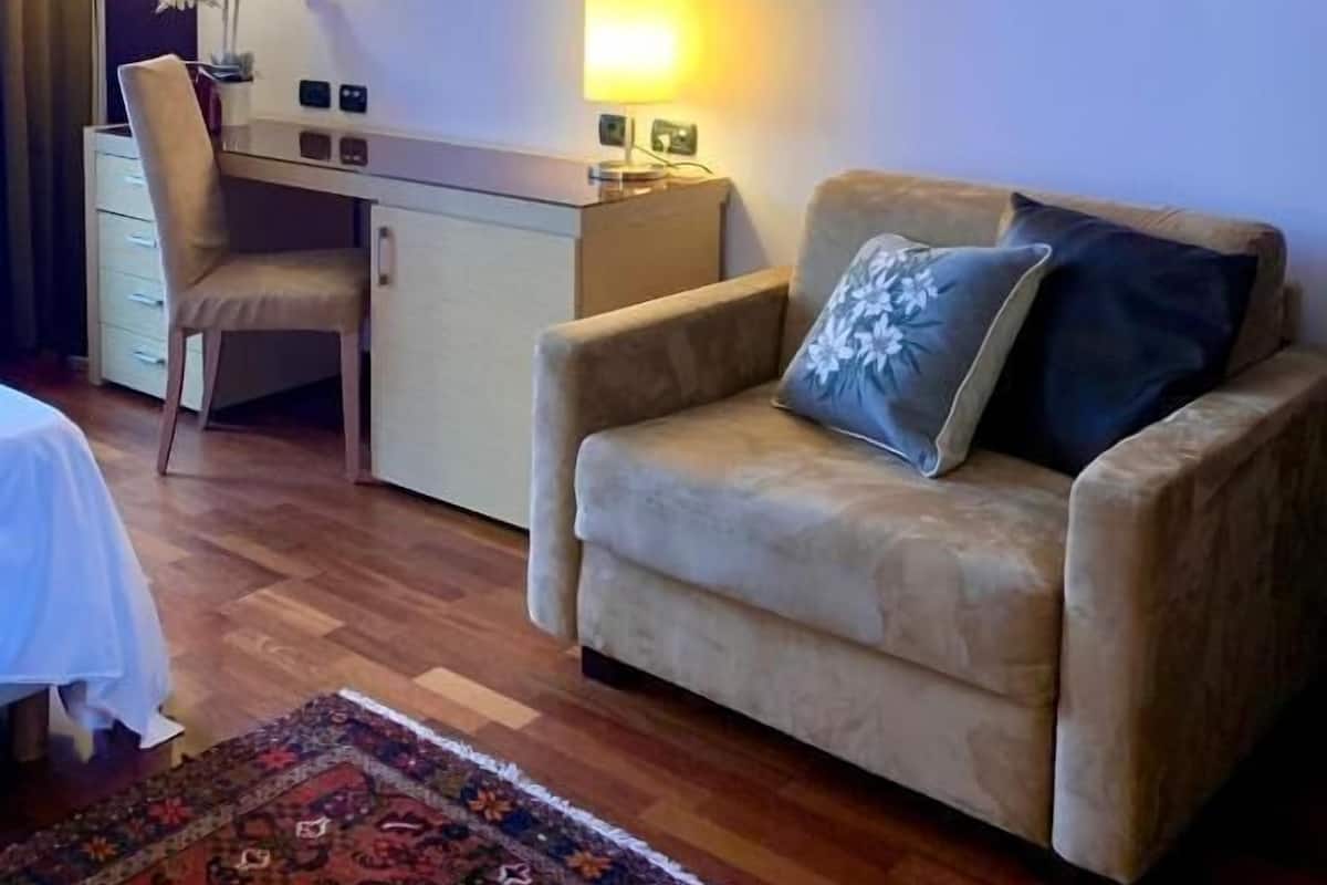 Une chambre d’hôtel équipée d’un bureau, d’une chaise, d’un canapé, d’une lampe et d’un tapis à motifs.