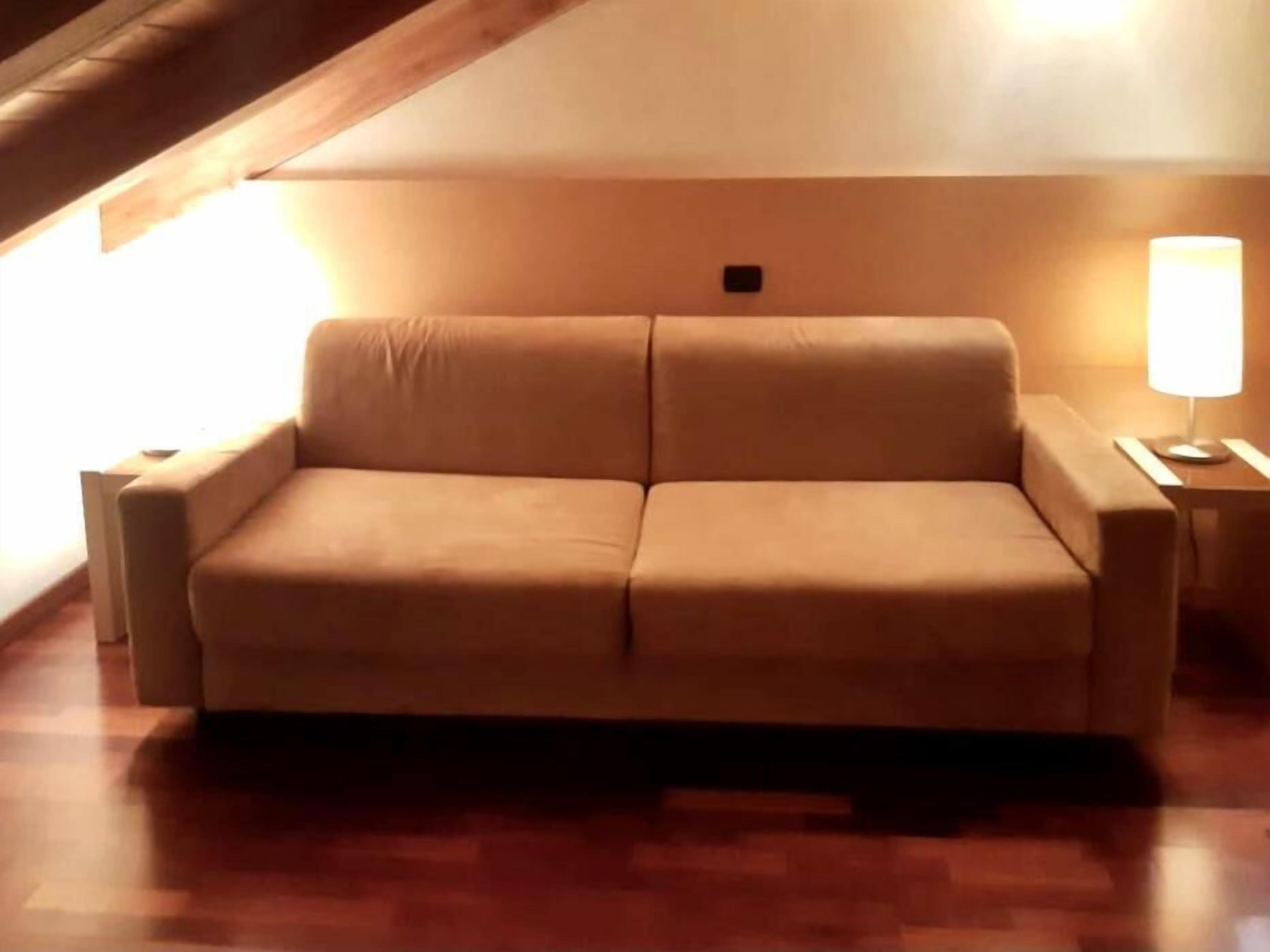 A tan sofa in a room with wooden flooring and a lamp on a side table.