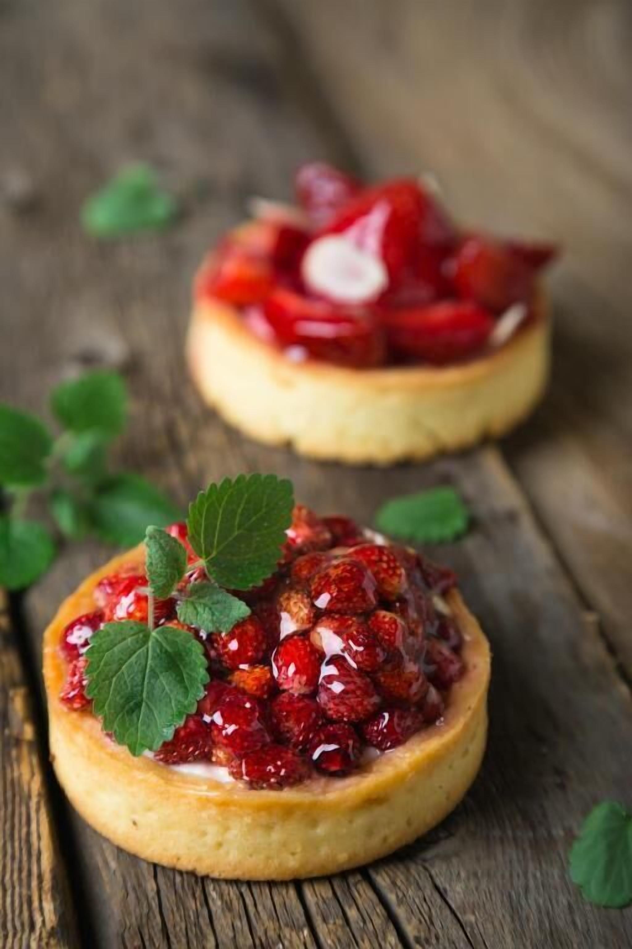 Two round pastries topped with red fruit compote and a mint leaf, placed on a wooden surface.