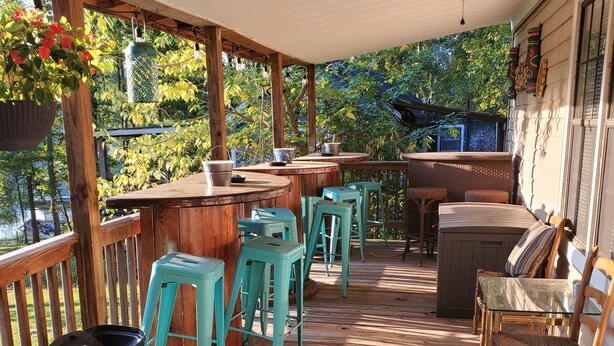 A covered outdoor deck with wooden flooring, a bar area, and seating.