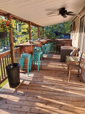A covered outdoor deck with wooden flooring, a bar area, and seating.