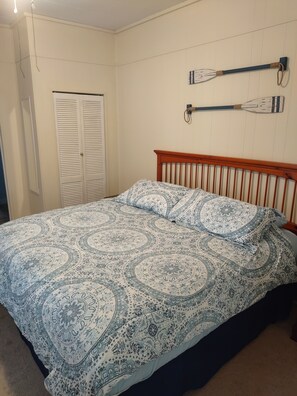 Un dormitorio con una cama, cabecero de madera, un armario blanco y dos palas fijadas a la pared.