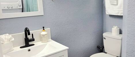 A bathroom with a white sink, a toilet, a mirror, and a window with blinds.