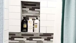 Une salle de bain avec un mur carrelé, une étagère contenant des articles de toilette et un rideau de douche.