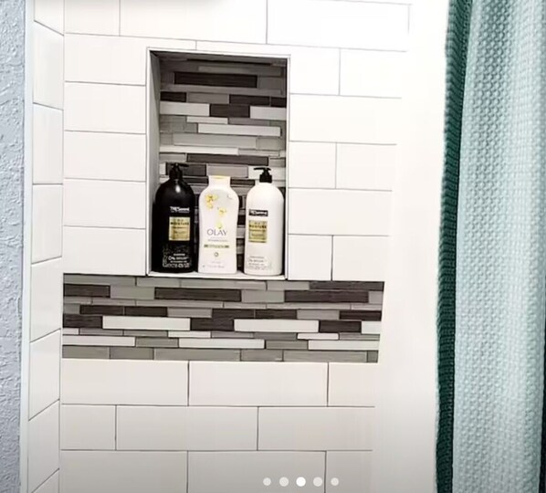 A bathroom with a tiled wall, a shelf with toiletries, and a shower curtain.