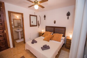 A bedroom with a bed, bedside tables, a ceiling fan, a mirror, and wall decorations.
