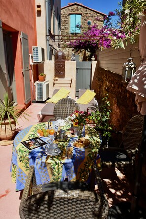An outdoor dining area with a table set for two, surrounded by wicker furniture and potted plants.