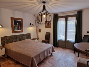 A hotel room with a bed, a desk, a chair, a dining table, and a large window with curtains.