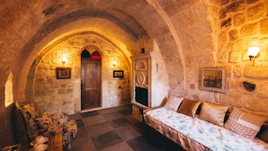 A cozy stone-walled room with a checkered floor, a wooden door, and a sofa with patterned cushions. - Cappadocia Old Houses (Ürgüp)