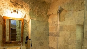 A bathroom with a stone wall, a bathtub, a sink, and a mirror. - Cappadocia Old Houses (Ürgüp)
