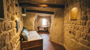 A narrow stone-walled room with a wooden bed, a small window, and a sloped ceiling. - Cappadocia Old Houses (Ürgüp)
