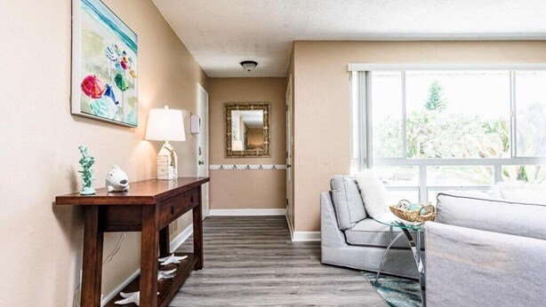 A hallway with a wooden console table, a lamp, a mirror, and a sofa with a glass coffee table. - Private 4 bedroom Pool Home w 2 car garage, Walk to the Beach, Dog Friendly (Ormond Beach)