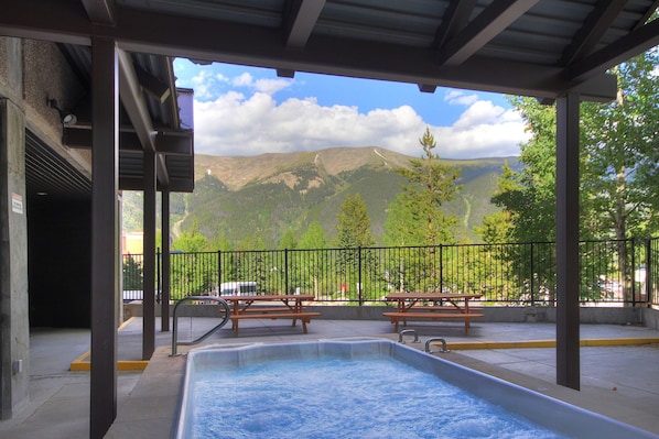 Un espace piscine extérieur abrité, avec vue sur les montagnes, des tables de pique-nique et une clôture.
