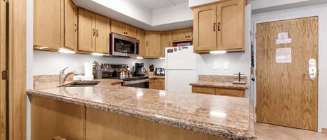 A kitchen with wooden cabinets, granite countertops, stainless steel appliances, and a built-in oven.