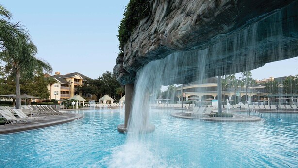 A pool with a waterfall feature, lounge chairs, and a building in the background. - Sheraton Vistana Resort in Orlando, Florida (includes Christmas weekend) (Orlando)