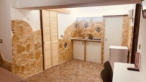 A compact kitchen with stone walls, a tiled floor, and a small dining area with a table and chairs. - Vacation Home PETRA (Modica)