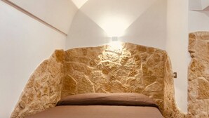 A room with a stone wall and a bed with a brown mattress. - Vacation Home PETRA (Modica)