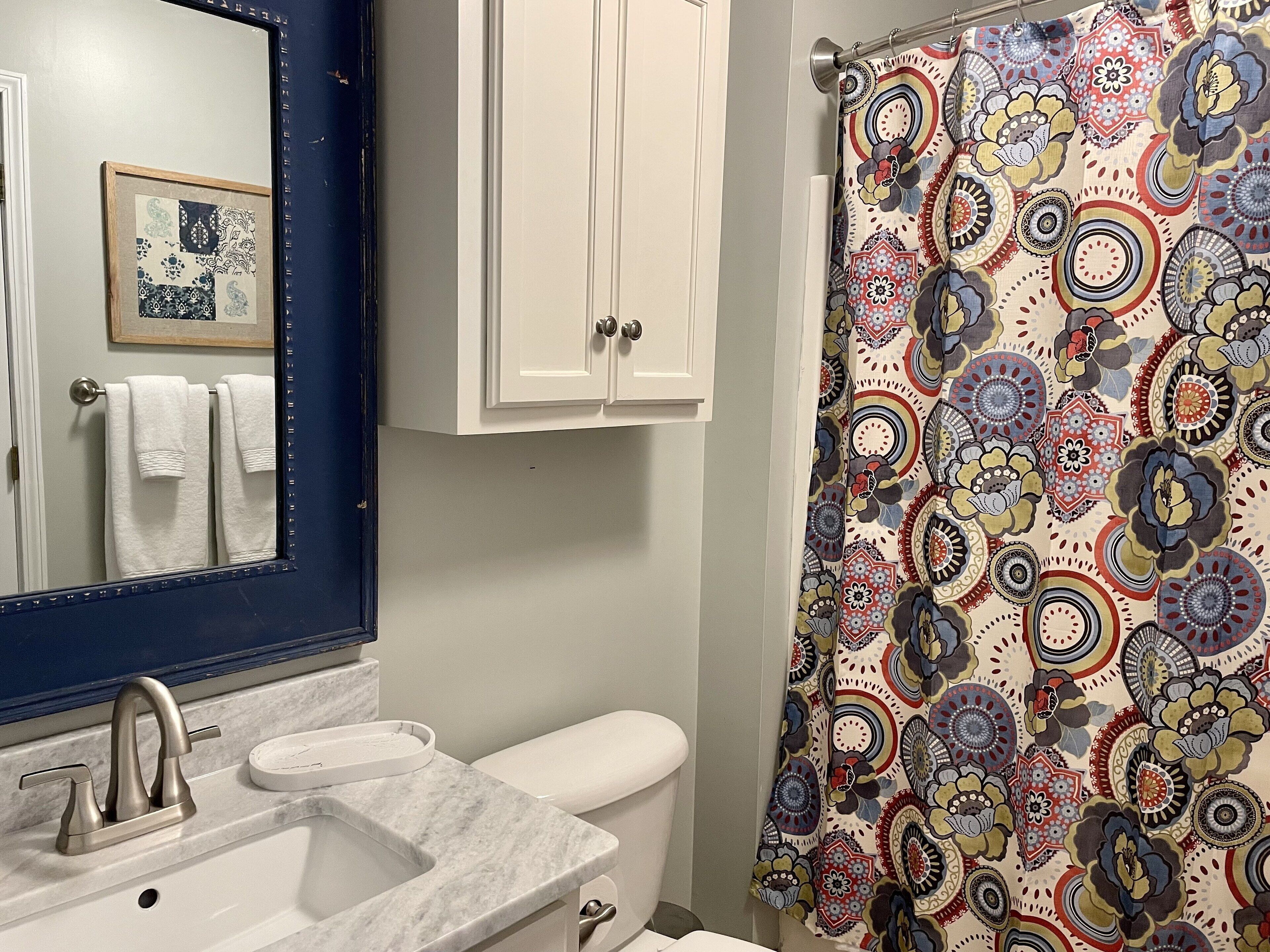 A bathroom with a white sink, a mirror, a toilet, and a shower curtain with a colorful floral pattern.