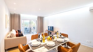 A modern living room with a dining area, a sofa, a TV, and a balcony view. - Comfortable apartment with pool in Albufeira (Albufeira)