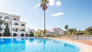 A swimming pool with clear blue water, surrounded by a white fence, and buildings with balconies in the background. - Comfortable apartment with pool in Albufeira (Albufeira)